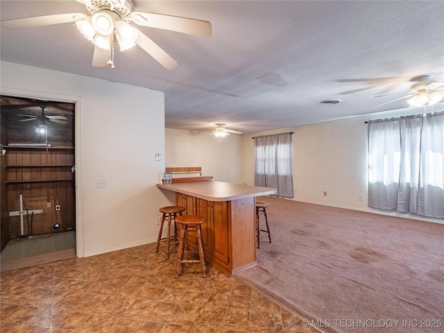 kitchen featuring a textured ceiling, a kitchen breakfast bar, kitchen peninsula, carpet floors, and ceiling fan