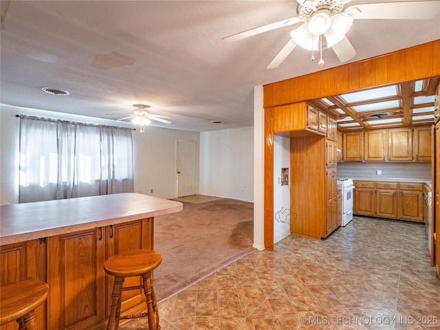 kitchen with gas range gas stove, ceiling fan, a breakfast bar, light carpet, and kitchen peninsula