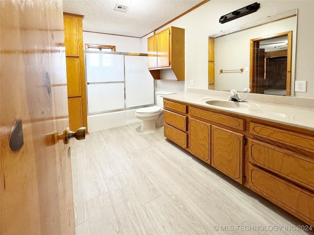 full bathroom featuring toilet, vanity, a textured ceiling, and combined bath / shower with glass door