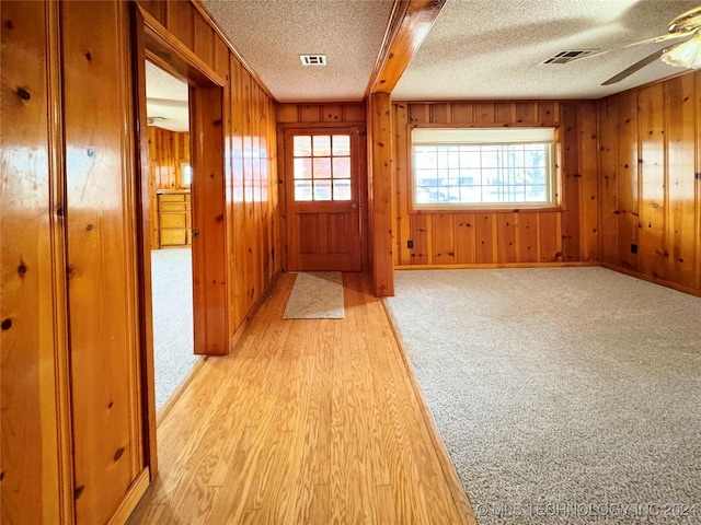 entryway featuring a textured ceiling, light hardwood / wood-style flooring, ceiling fan, and wood walls