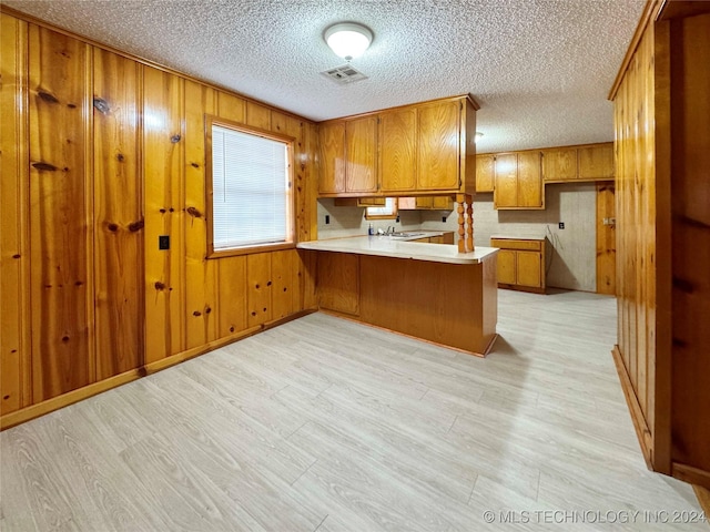 kitchen with kitchen peninsula, a textured ceiling, light hardwood / wood-style floors, and wood walls