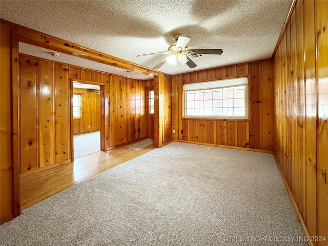 empty room featuring a textured ceiling, light hardwood / wood-style floors, ceiling fan, and wood walls