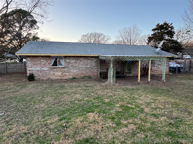 back of property at dusk with brick siding, fence, a patio, and a yard