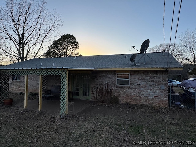 back of house at dusk featuring a patio, brick siding, and a shingled roof