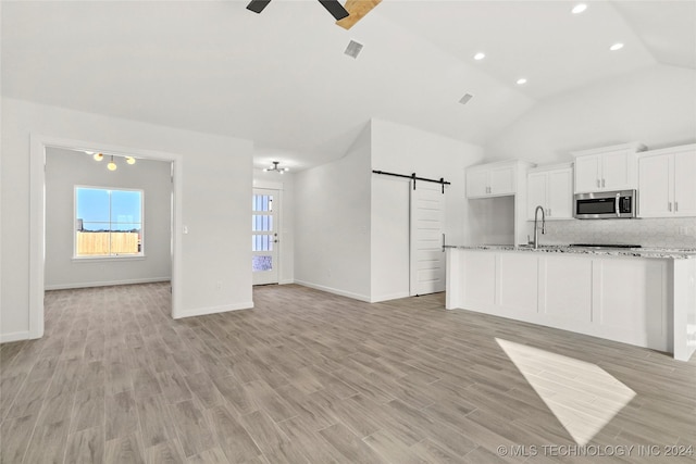 kitchen with white cabinets, vaulted ceiling, a barn door, light wood-type flooring, and light stone counters