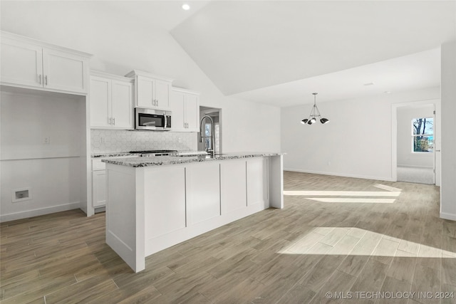 kitchen with a center island with sink, vaulted ceiling, light wood-type flooring, light stone counters, and white cabinetry