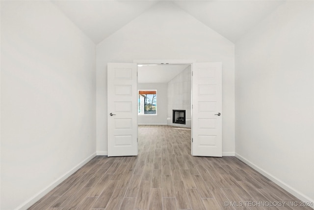 spare room with a tile fireplace, light hardwood / wood-style floors, and vaulted ceiling