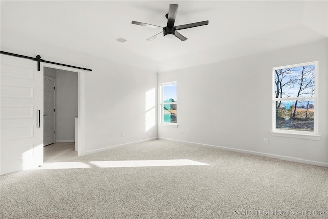 spare room featuring ceiling fan, a barn door, and light colored carpet