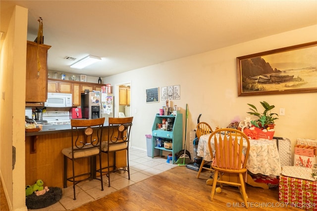 kitchen with a kitchen breakfast bar, kitchen peninsula, light hardwood / wood-style floors, and white appliances