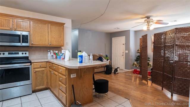 kitchen with ceiling fan, a kitchen breakfast bar, kitchen peninsula, light hardwood / wood-style floors, and appliances with stainless steel finishes