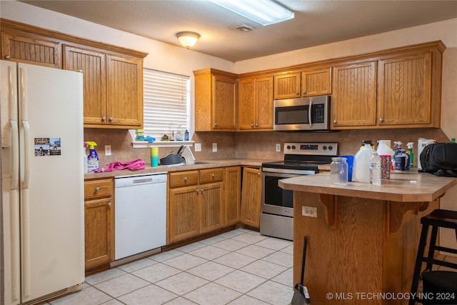 kitchen featuring sink, stainless steel appliances, a kitchen breakfast bar, kitchen peninsula, and light tile patterned floors