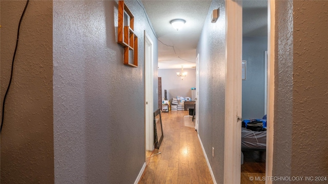 hall featuring a textured ceiling, light hardwood / wood-style floors, and a notable chandelier