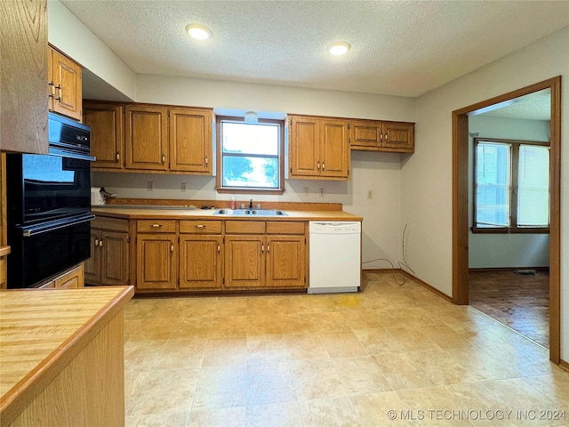 kitchen featuring a textured ceiling, white dishwasher, double oven, and sink