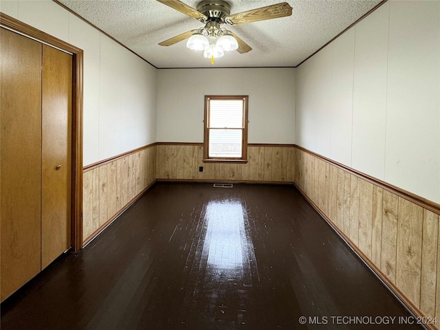 spare room with dark hardwood / wood-style floors, wood walls, and a textured ceiling