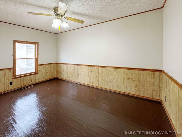 empty room featuring a textured ceiling, ceiling fan, dark wood-type flooring, and wooden walls