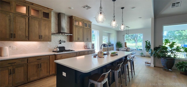 kitchen featuring a center island with sink, wall chimney exhaust hood, sink, and a breakfast bar area