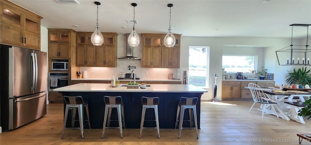 kitchen with backsplash, a kitchen island with sink, wall chimney exhaust hood, a kitchen bar, and stainless steel appliances