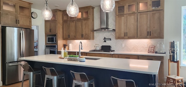 kitchen featuring stainless steel appliances, wall chimney range hood, backsplash, a breakfast bar, and a center island with sink