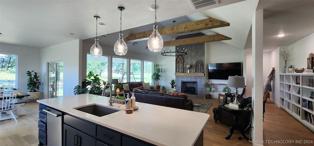 kitchen with sink, lofted ceiling with beams, pendant lighting, a kitchen island with sink, and a fireplace