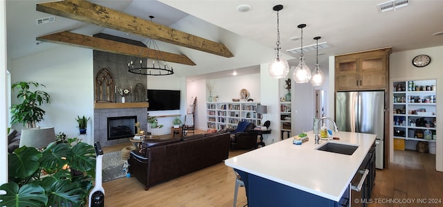 kitchen featuring pendant lighting, a breakfast bar, a tile fireplace, sink, and an island with sink