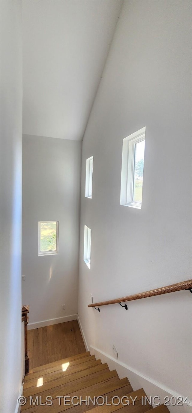 stairway with wood-type flooring and high vaulted ceiling