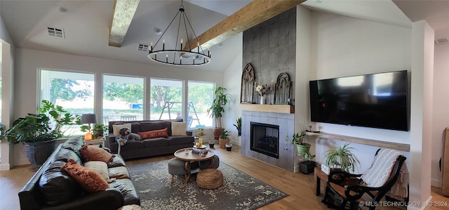 living room featuring beam ceiling, an inviting chandelier, high vaulted ceiling, a tiled fireplace, and light wood-type flooring