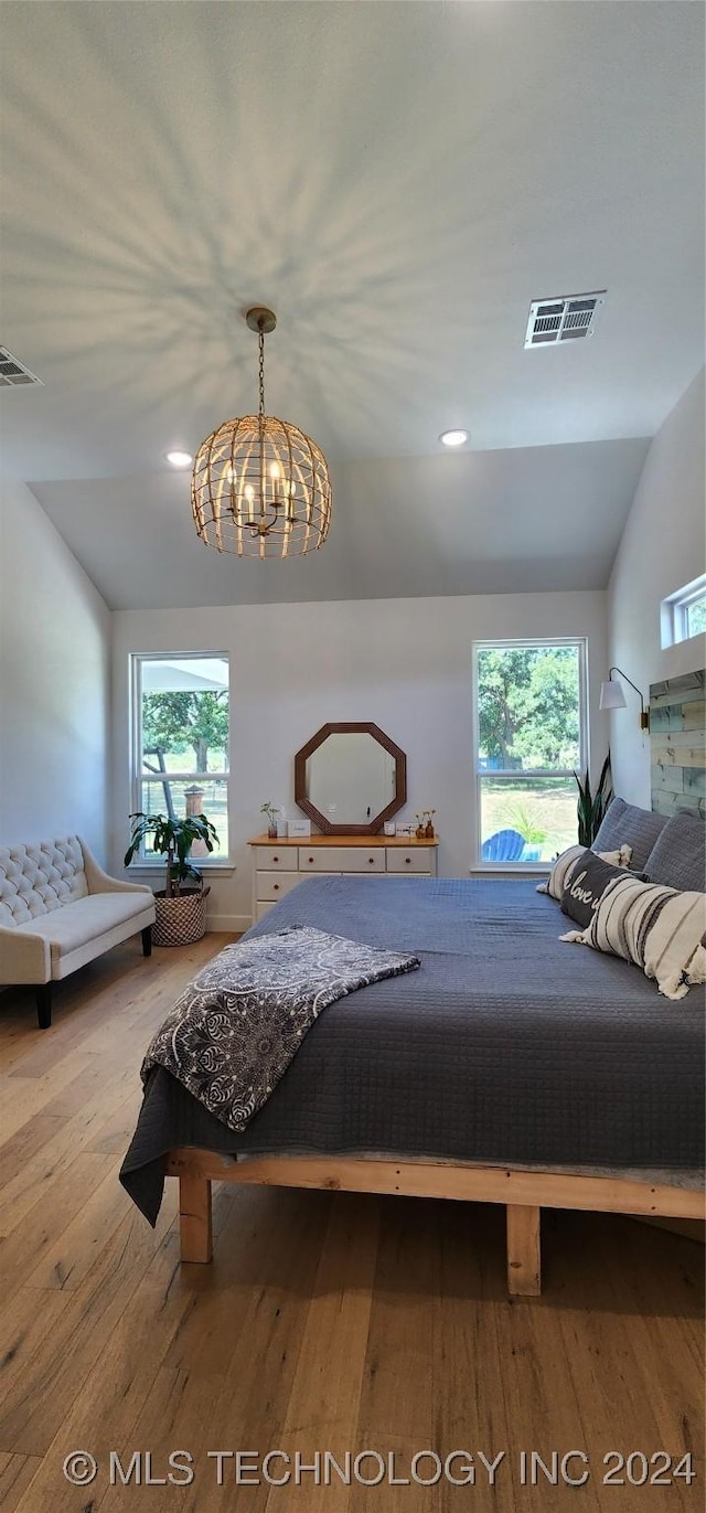 bedroom featuring an inviting chandelier, light hardwood / wood-style floors, multiple windows, and vaulted ceiling