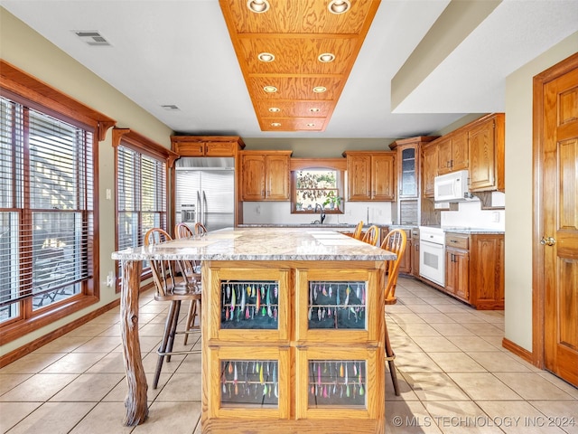 kitchen featuring a breakfast bar, white appliances, sink, a kitchen island, and light tile patterned flooring