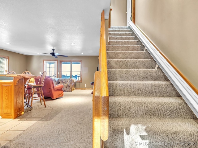 staircase with ceiling fan, carpet floors, and a textured ceiling