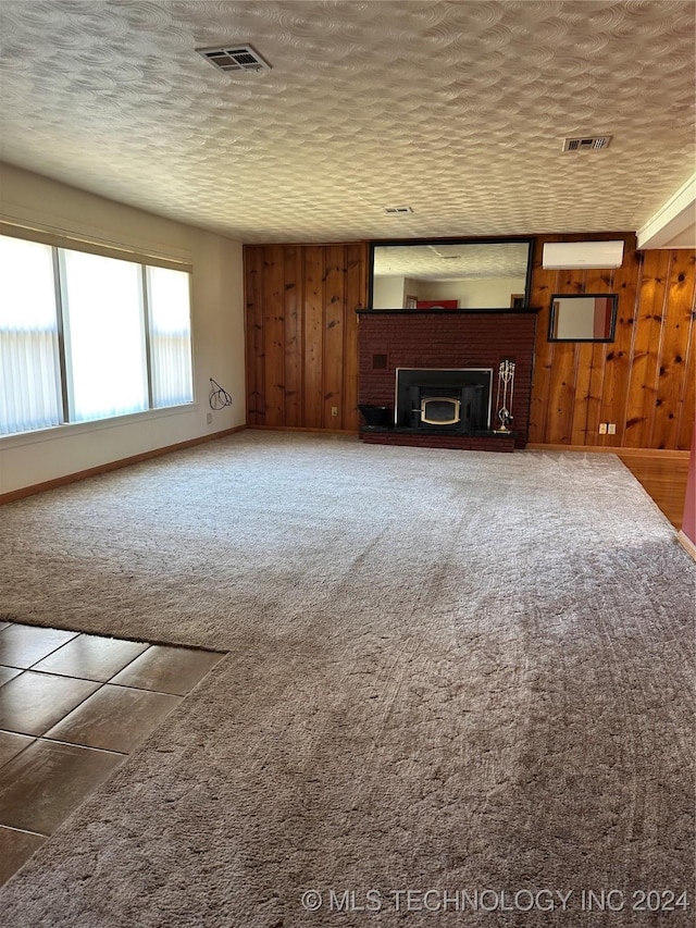 unfurnished living room with carpet, a brick fireplace, wooden walls, and a textured ceiling