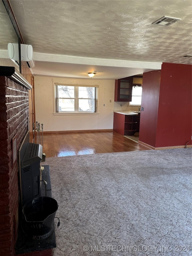 unfurnished living room with a fireplace, hardwood / wood-style floors, a textured ceiling, and a wall mounted air conditioner