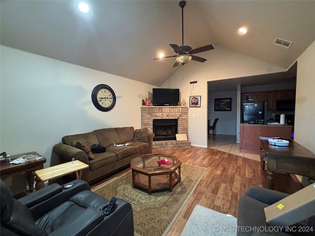 living room featuring a brick fireplace, light wood-type flooring, vaulted ceiling, and ceiling fan