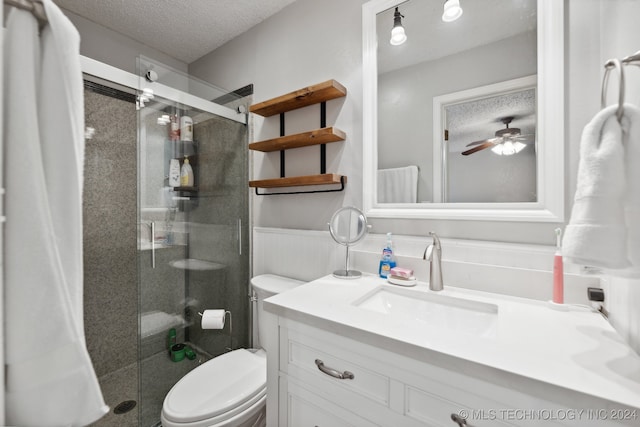 bathroom with ceiling fan, a textured ceiling, toilet, a shower with door, and vanity