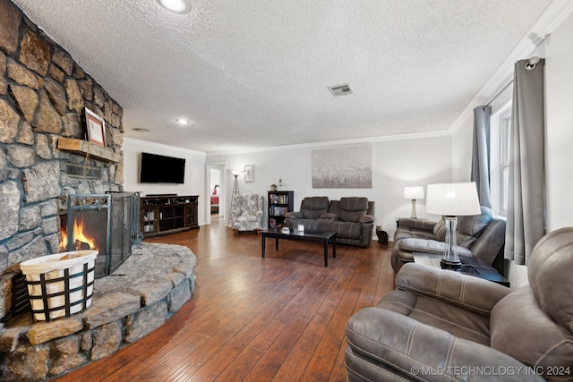 living room with a textured ceiling, a stone fireplace, wood-type flooring, and crown molding