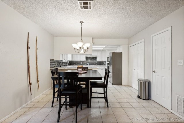 tiled dining area featuring a textured ceiling, sink, and an inviting chandelier