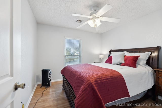 bedroom with ceiling fan, wood-type flooring, and a textured ceiling