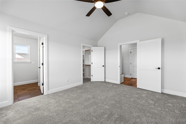 unfurnished bedroom with dark colored carpet, a walk in closet, ceiling fan, and lofted ceiling