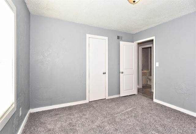 unfurnished bedroom with dark colored carpet and a textured ceiling