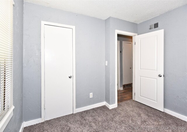 unfurnished bedroom with dark carpet and a textured ceiling