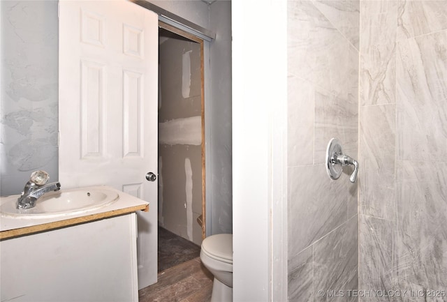 bathroom featuring wood-type flooring, toilet, vanity, and a tile shower