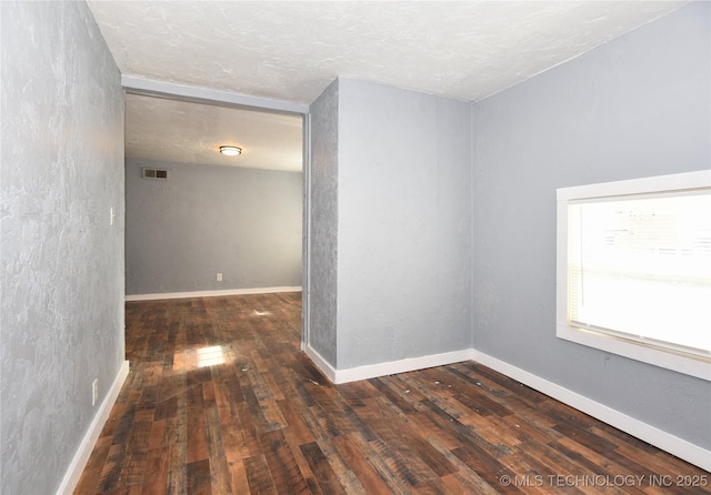 empty room with dark wood-type flooring and a textured ceiling