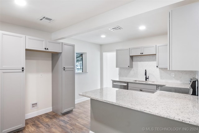 kitchen featuring light stone counters, stainless steel dishwasher, sink, hardwood / wood-style floors, and gray cabinets