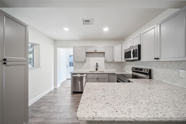 kitchen with appliances with stainless steel finishes, tasteful backsplash, gray cabinetry, sink, and hardwood / wood-style flooring