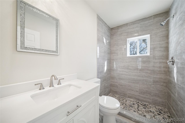 bathroom featuring a tile shower, vanity, and toilet