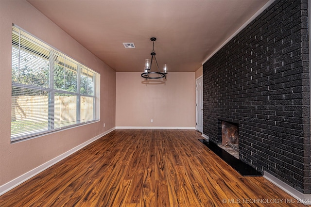 unfurnished living room featuring hardwood / wood-style flooring, an inviting chandelier, and a brick fireplace