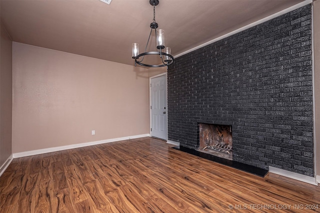 unfurnished living room with a fireplace, wood-type flooring, a notable chandelier, and brick wall