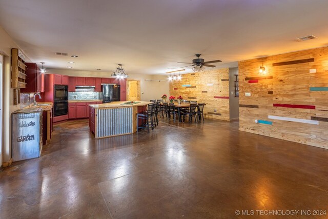 kitchen with ceiling fan, a center island, sink, wooden walls, and black appliances