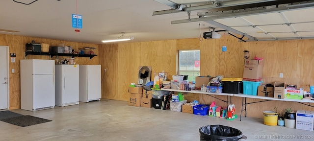 garage with white refrigerator, a garage door opener, and wood walls