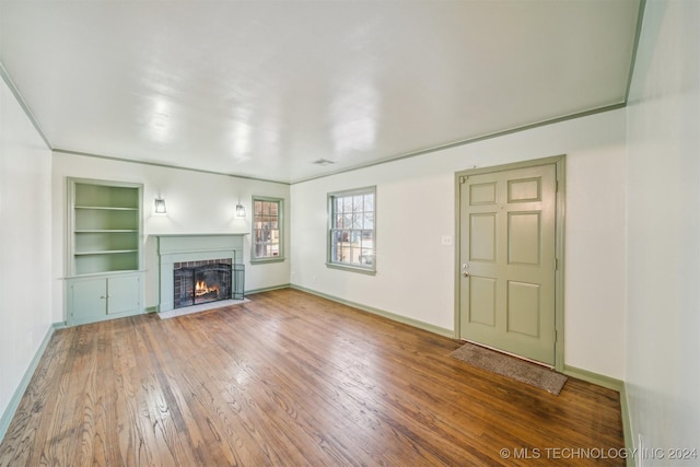 unfurnished living room featuring built in shelves and hardwood / wood-style flooring