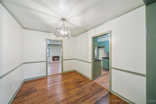 unfurnished dining area with hardwood / wood-style floors, crown molding, a fireplace, and an inviting chandelier